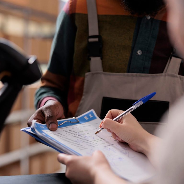 Supervisor signing merchandise quality control report, discussing customers online orders before start preparing packages. Diverse team analyzing goods checklist in warehouse. Close up